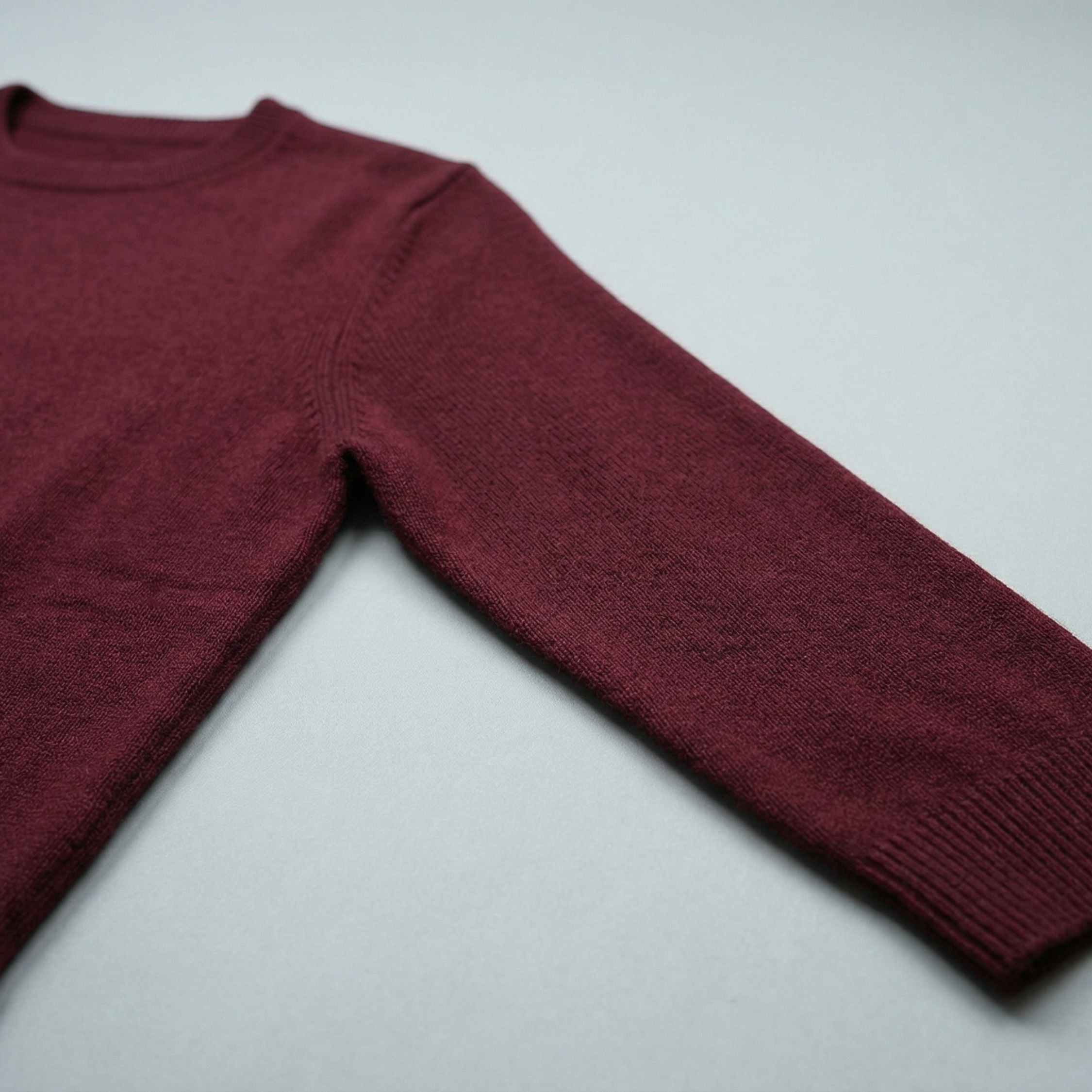 Close-up of an maroon red 2-ply cashmere 3 Quarter Sweater, showcasing the fine 13-gauge single jersey stitch and a ribbed crewneck along the neckline, ribbed cuffs, hems and the 3 Quarter length sleeve. 