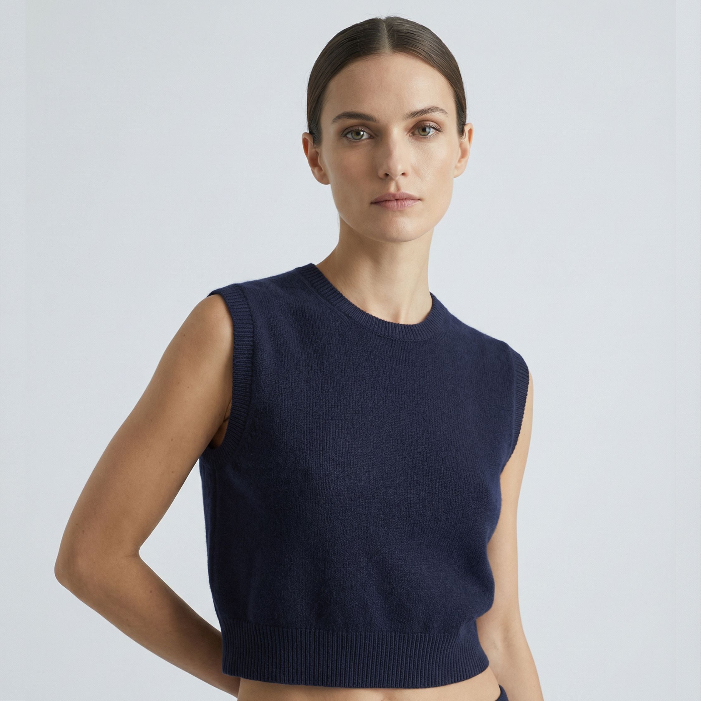 Female model wearing a navy blue, sleeveless knitted crop top made of 100% cashmere pashmina, paired with navy trousers.