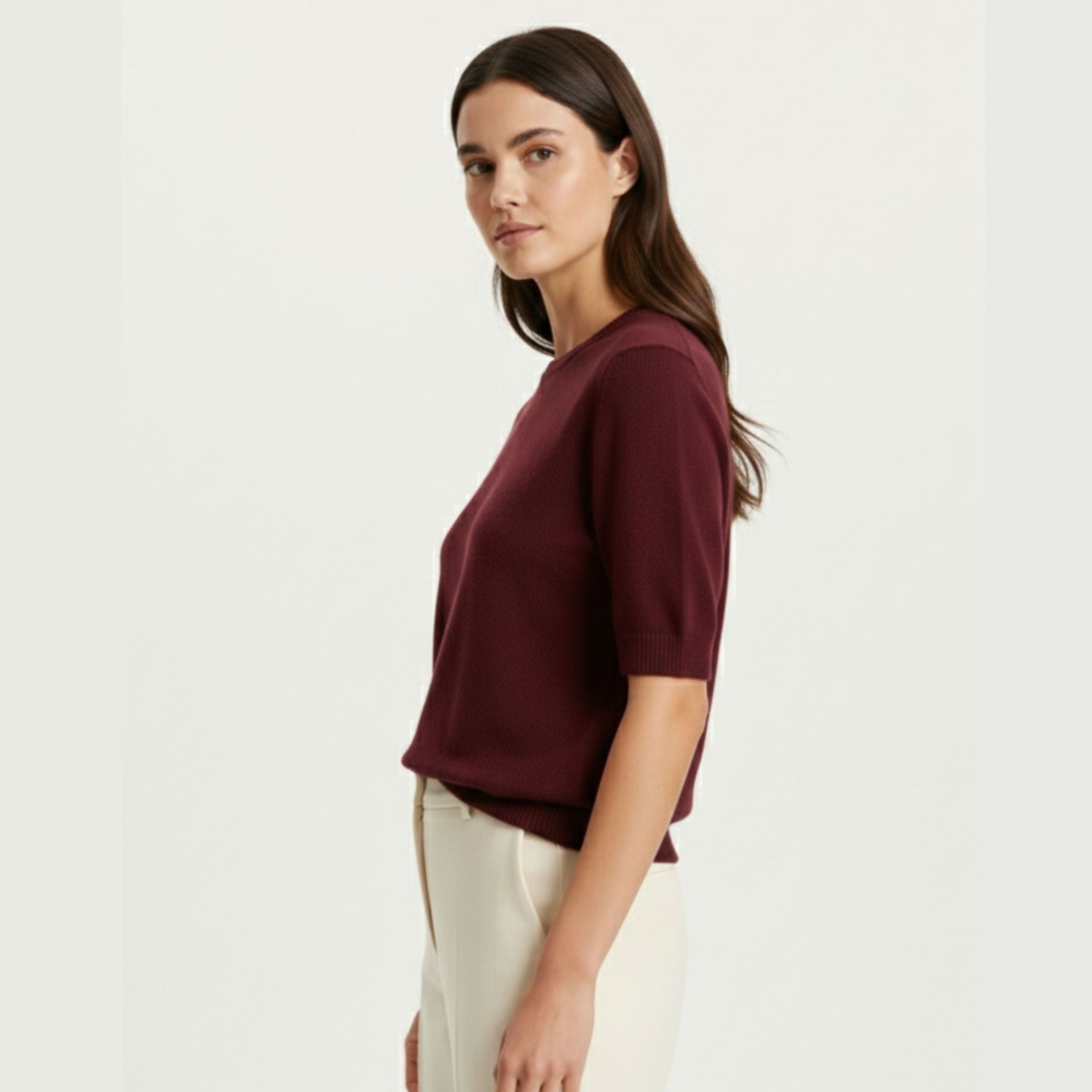 Female model wearing a Maroon Red regular-fit knitted T-shirt made of 100% cashmere pashmina, paired with white trousers.