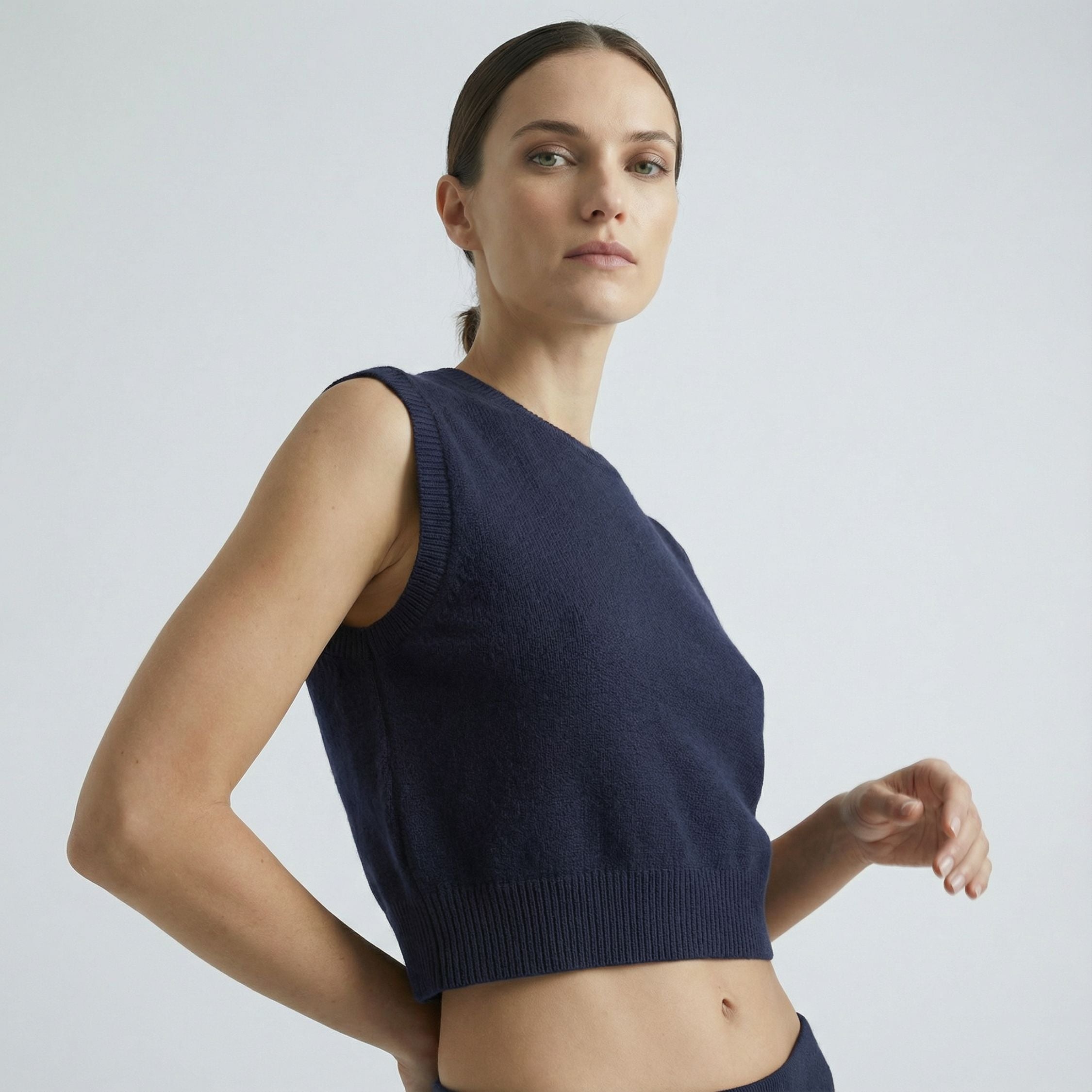 Female model wearing a navy blue, sleeveless knitted crop top made of 100% cashmere pashmina, paired with navy trousers.