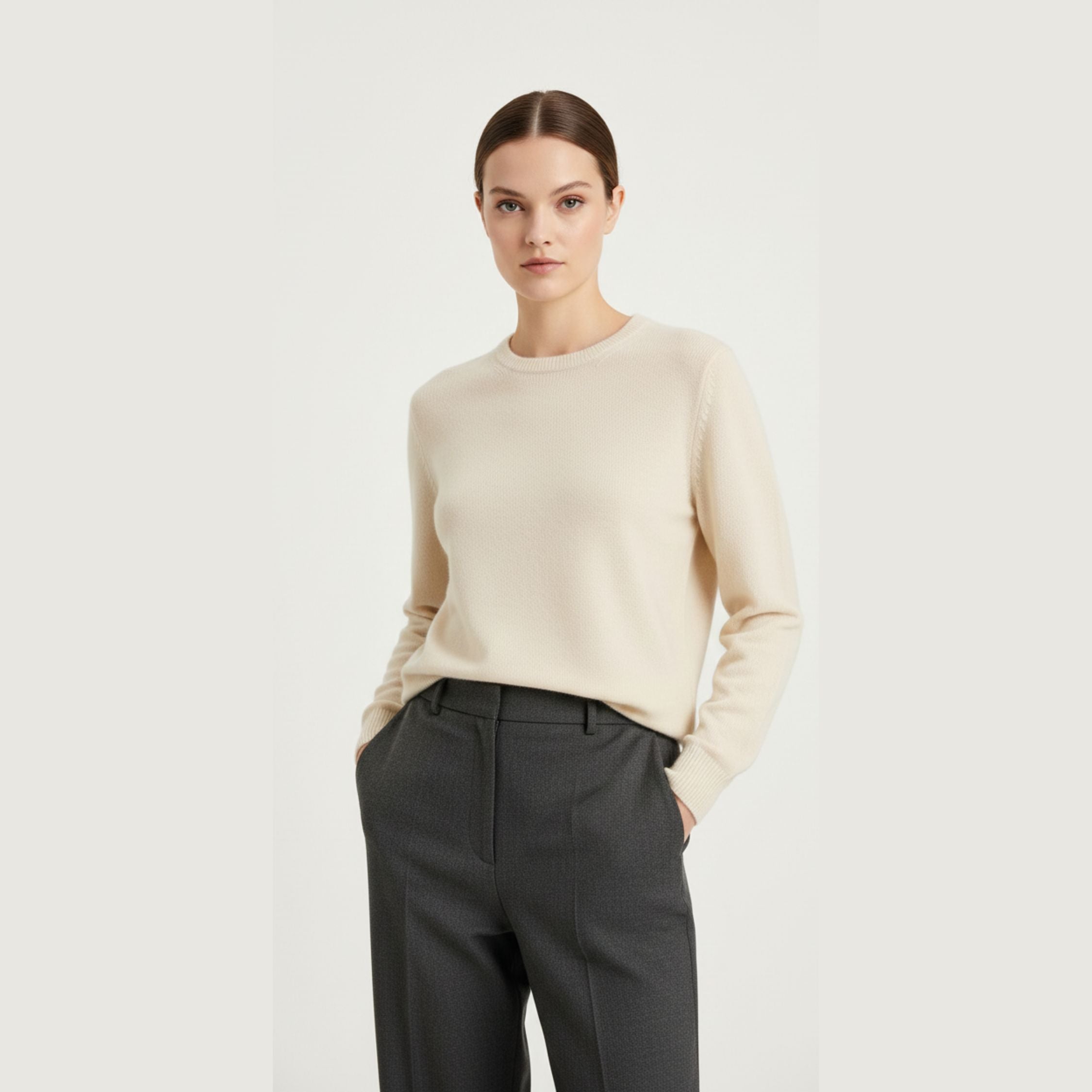 Female model wearing a cream white, regular-fit knitted sweater made of 100% cashmere pashmina, paired with dark grey trousers.