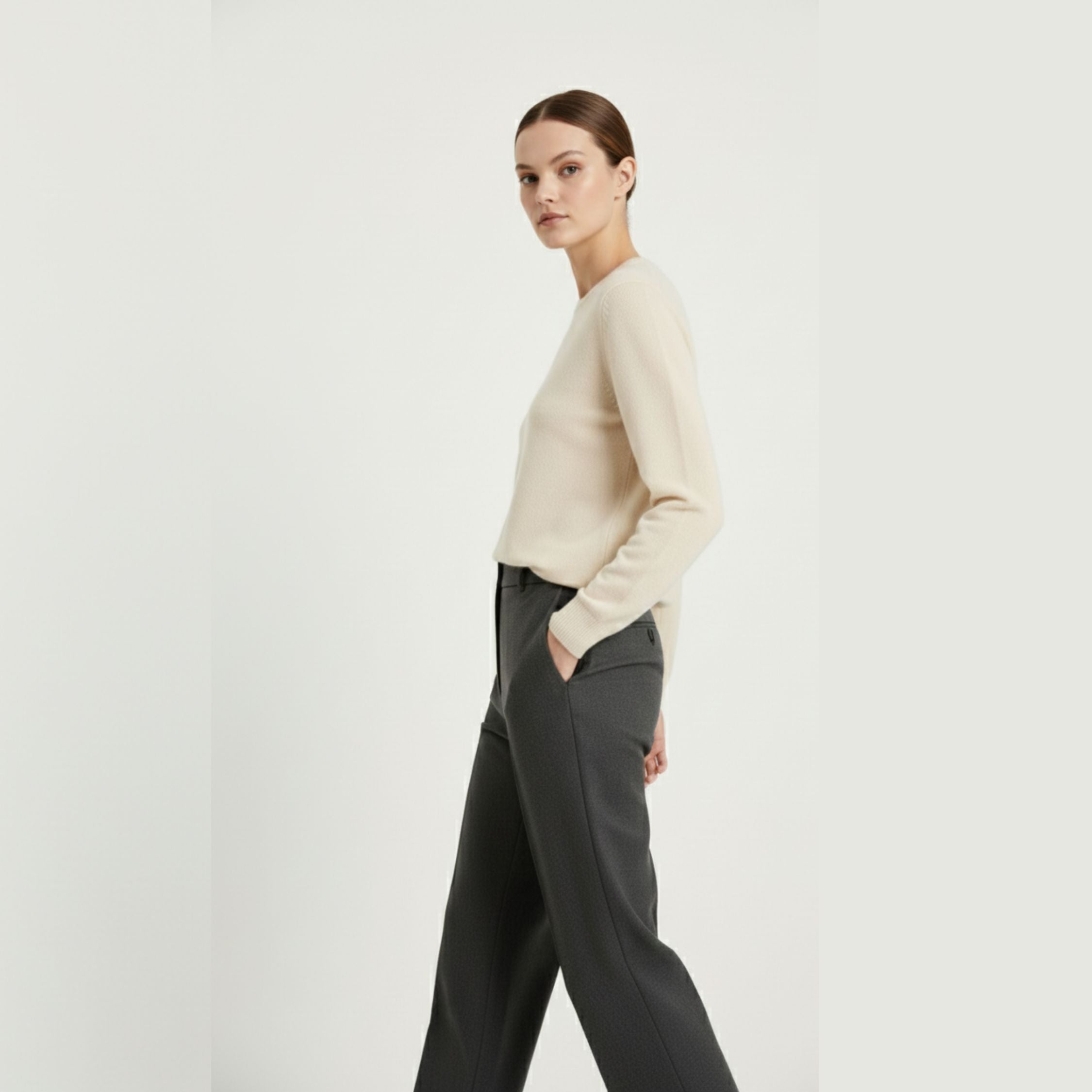 Female model wearing a cream white, regular-fit knitted sweater made of 100% cashmere pashmina, paired with dark grey trousers.