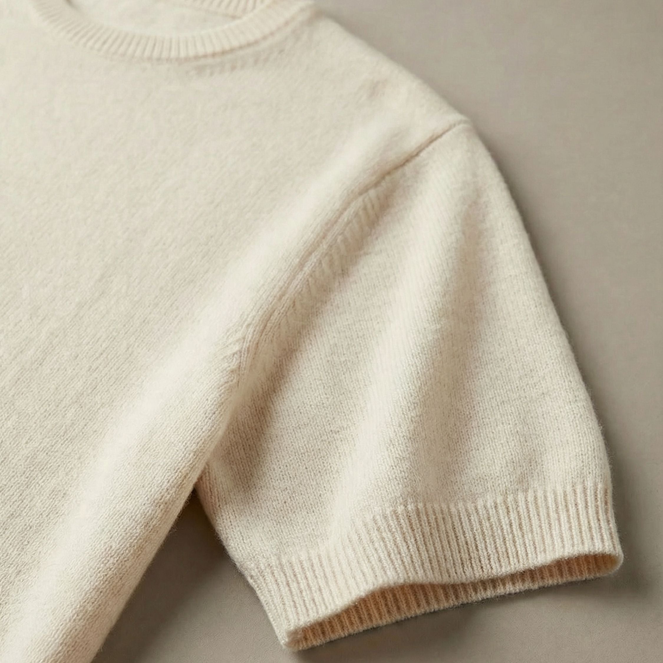 Close-up of an cream white 2-ply cashmere knitted t-shirt, showcasing the fine 13-gauge single jersey stitch and a ribbed crewneck along the neckline, ribbed cuffs and hem.