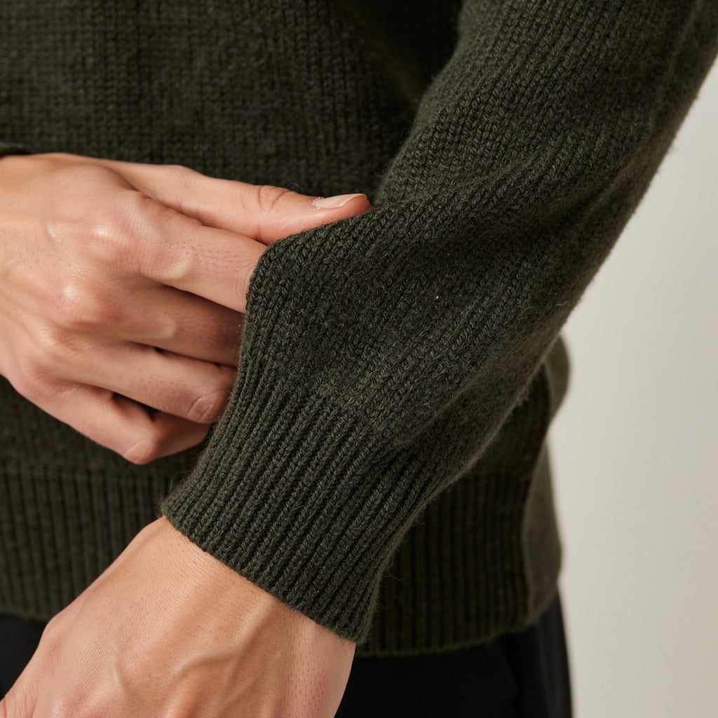 Close-up of a person wearing a dark green 100% Cashmere sweater with a neutral background.