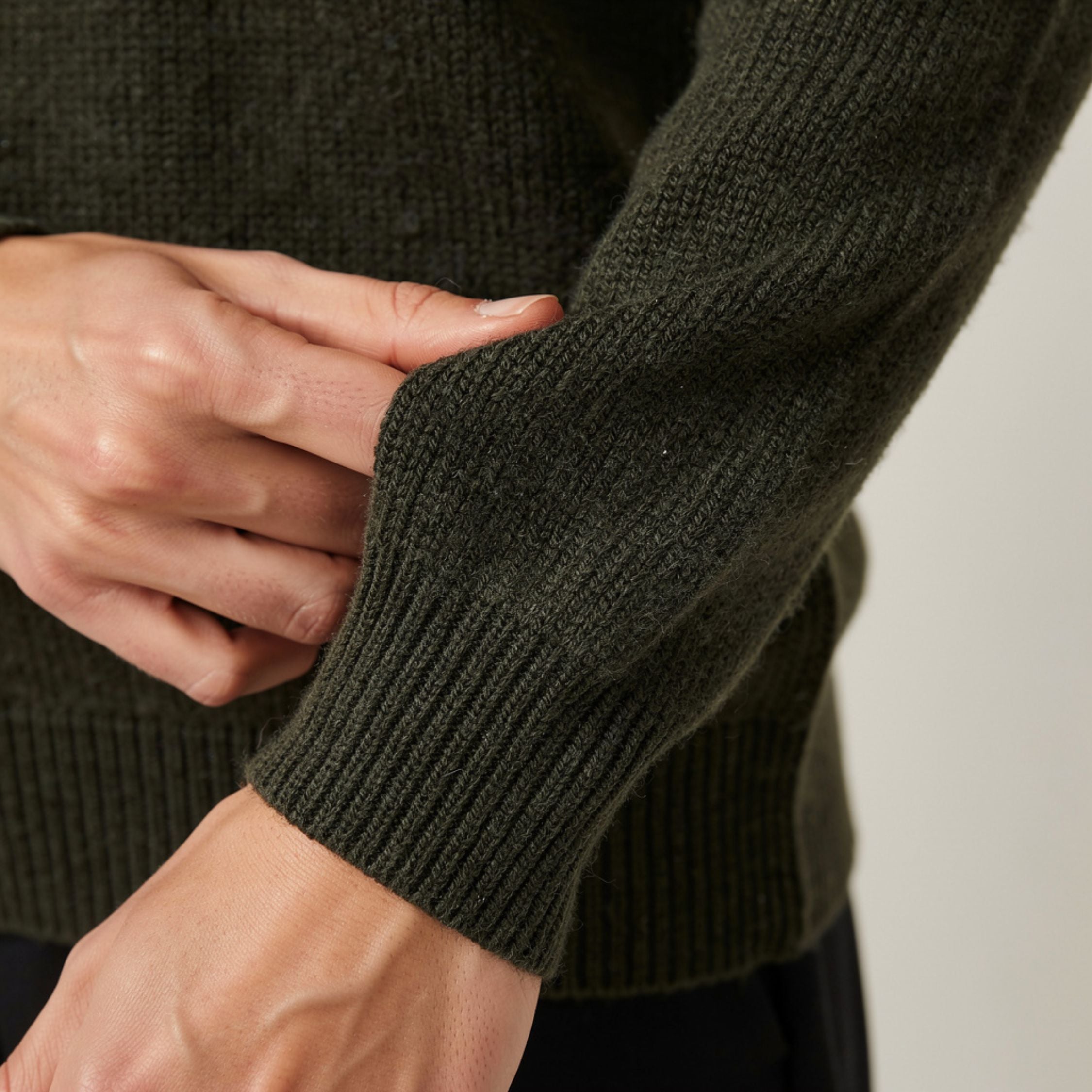 Close-up of a person wearing a dark green 100% Cashmere sweater with a neutral background.