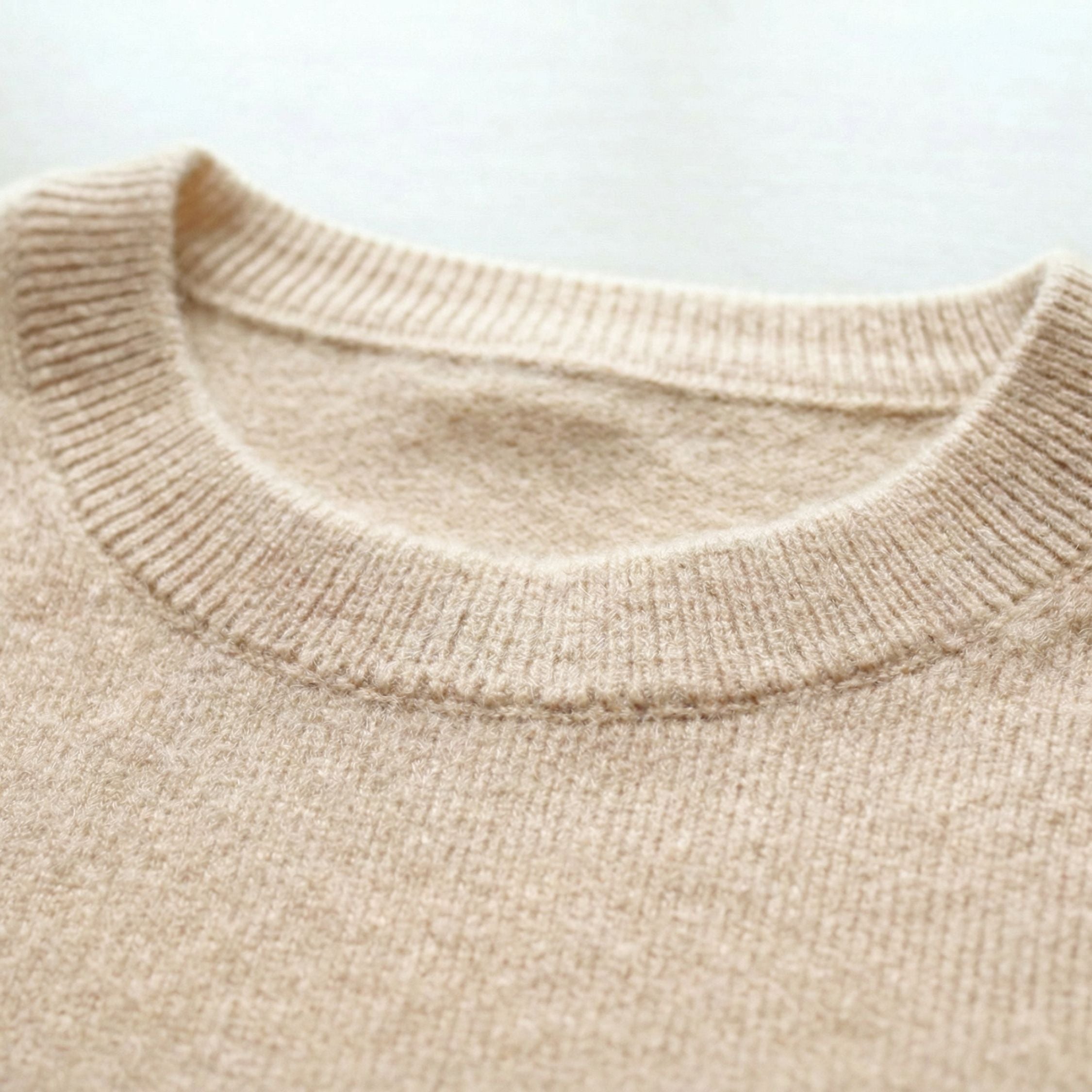 Close-up of an cream white 2-ply cashmere crewneck Sweater, showcasing the fine 13-gauge single jersey stitch and a ribbed crewneck along the neckline.