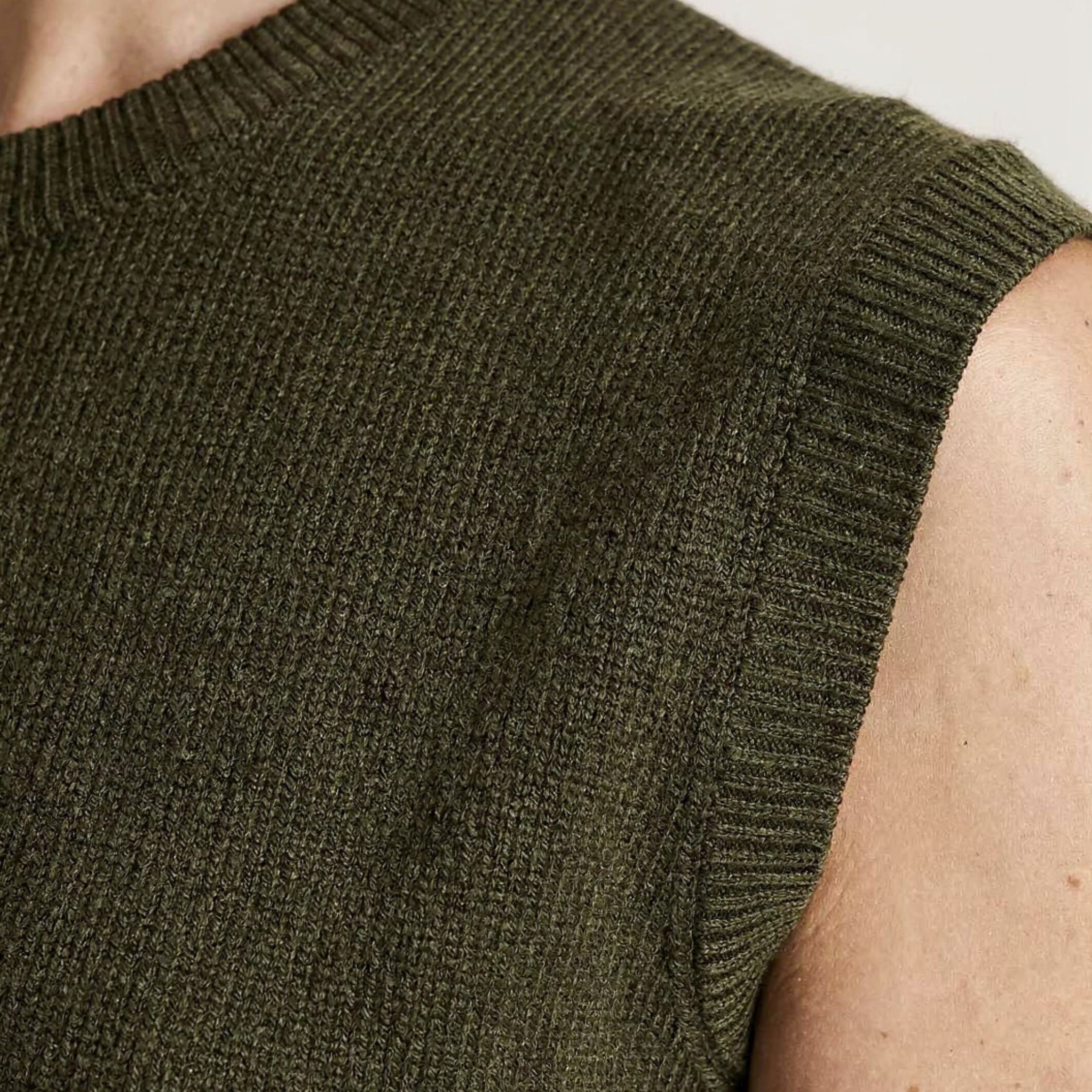 Close-up of a person wearing a green knitted sleeveless 100% cashmere sweater against a neutral background.