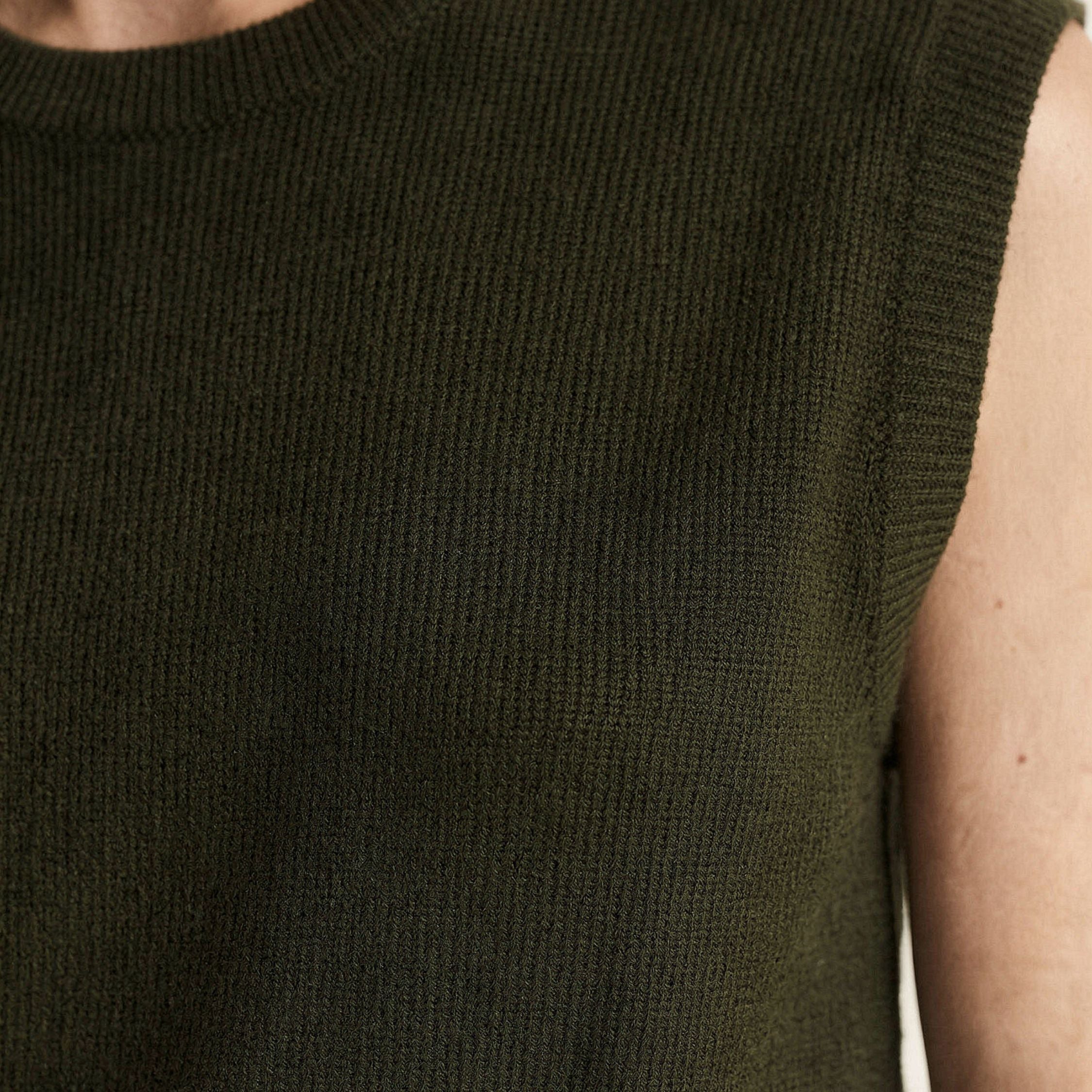 Close-up of a person wearing a dark green 100% cashmere sleeveless knitted top.