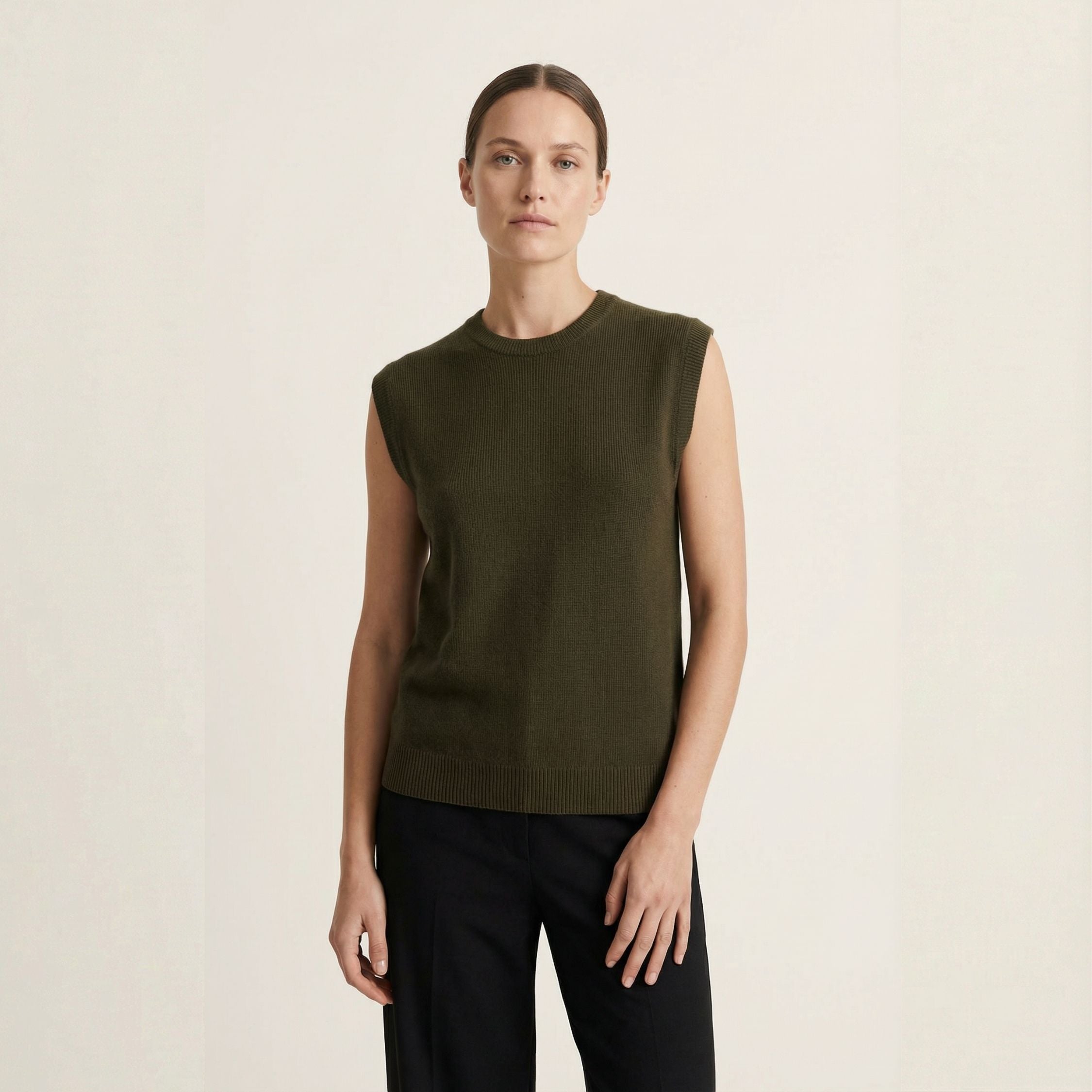 Woman wearing a green sleeveless 100% cashmere vest against a beige background.