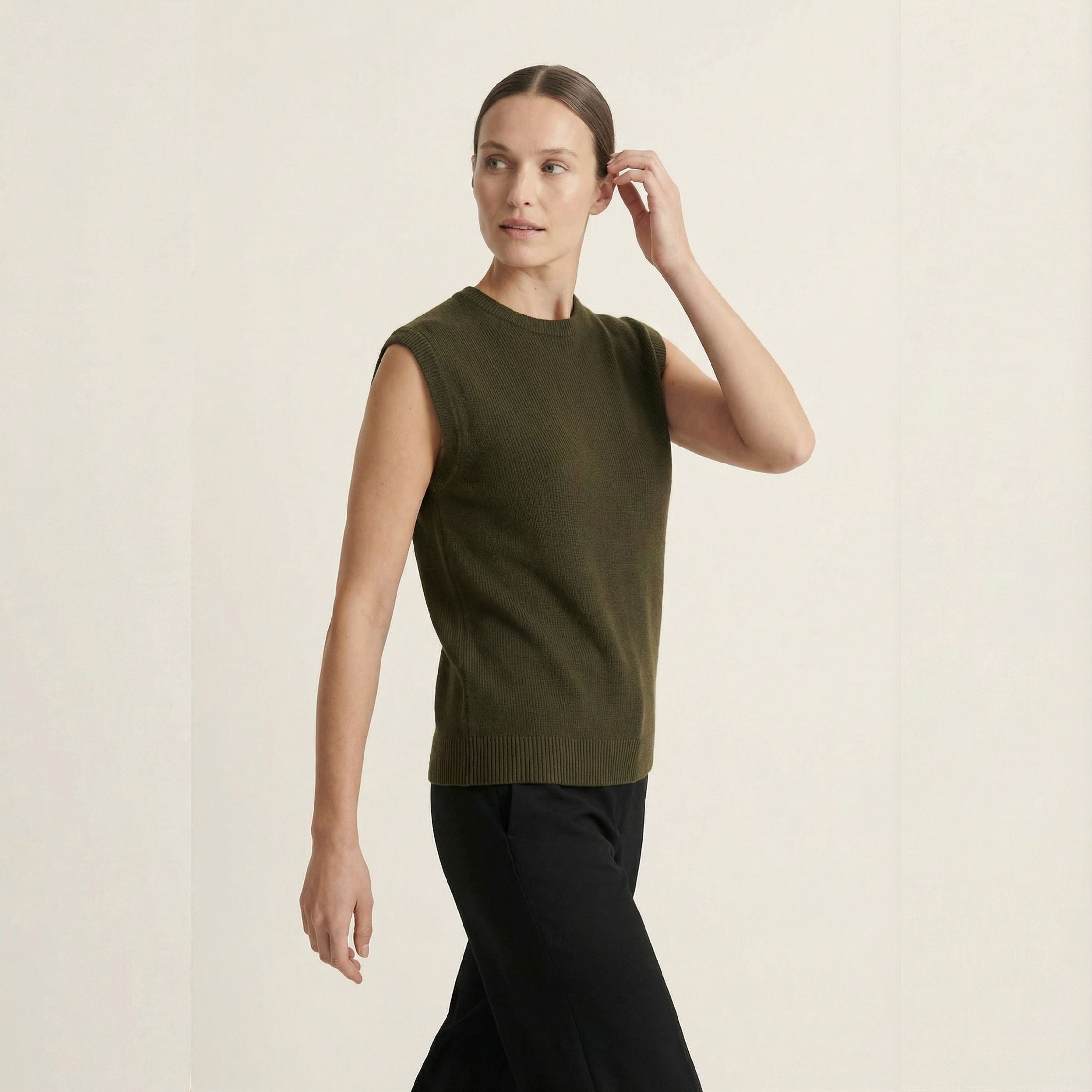 Woman wearing a green 100% cashmere sleeveless top and black pants on a beige background.