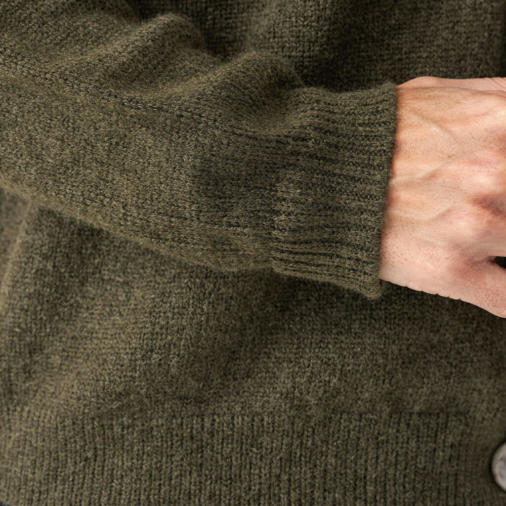 Close-up of a person wearing a green knitted 100% cashmere sweater with a button visible.