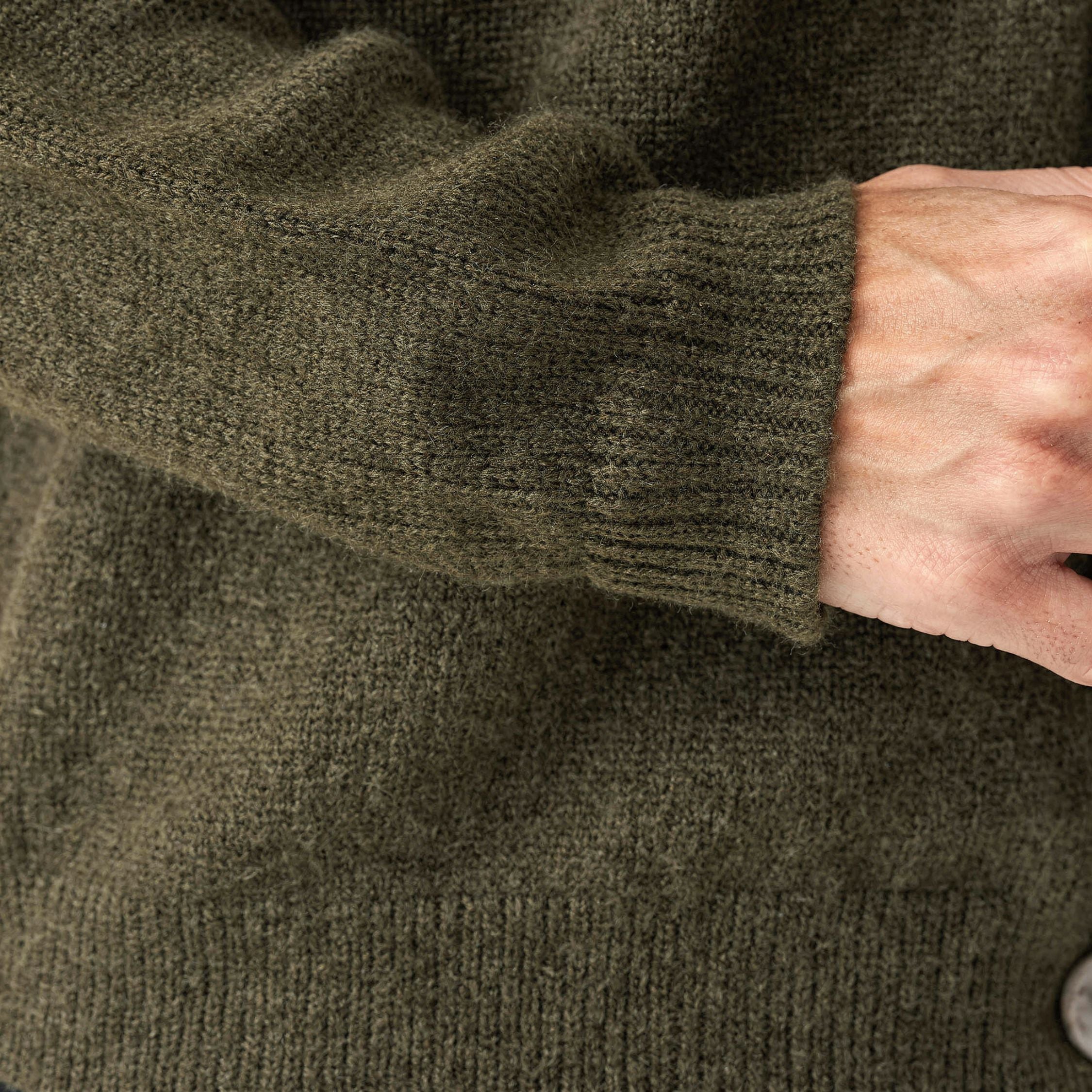 Close-up of a person wearing a green knitted 100% cashmere sweater with a button visible.