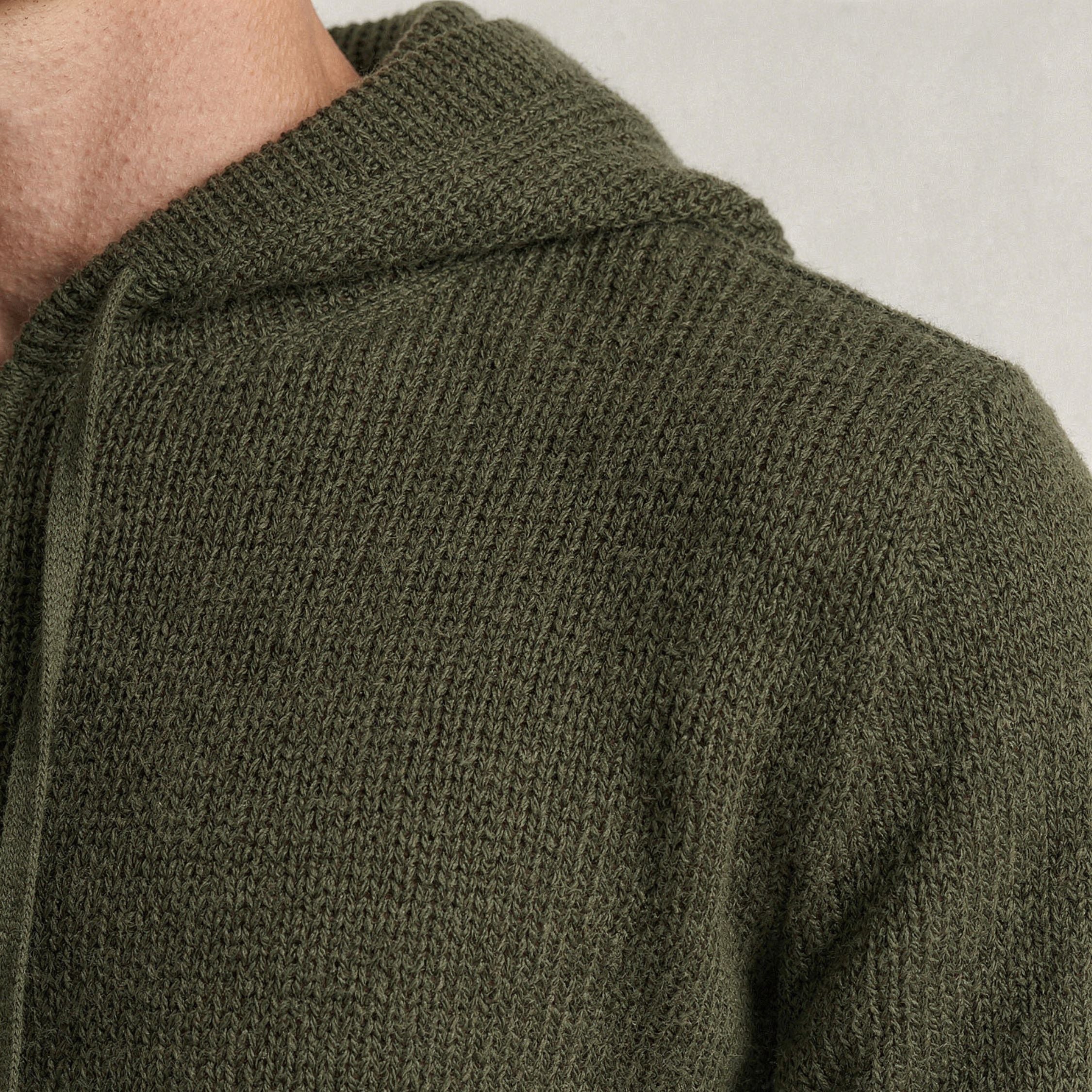 Close-up of a green knitted 100% cashmere sweater with a hood on a neutral background.