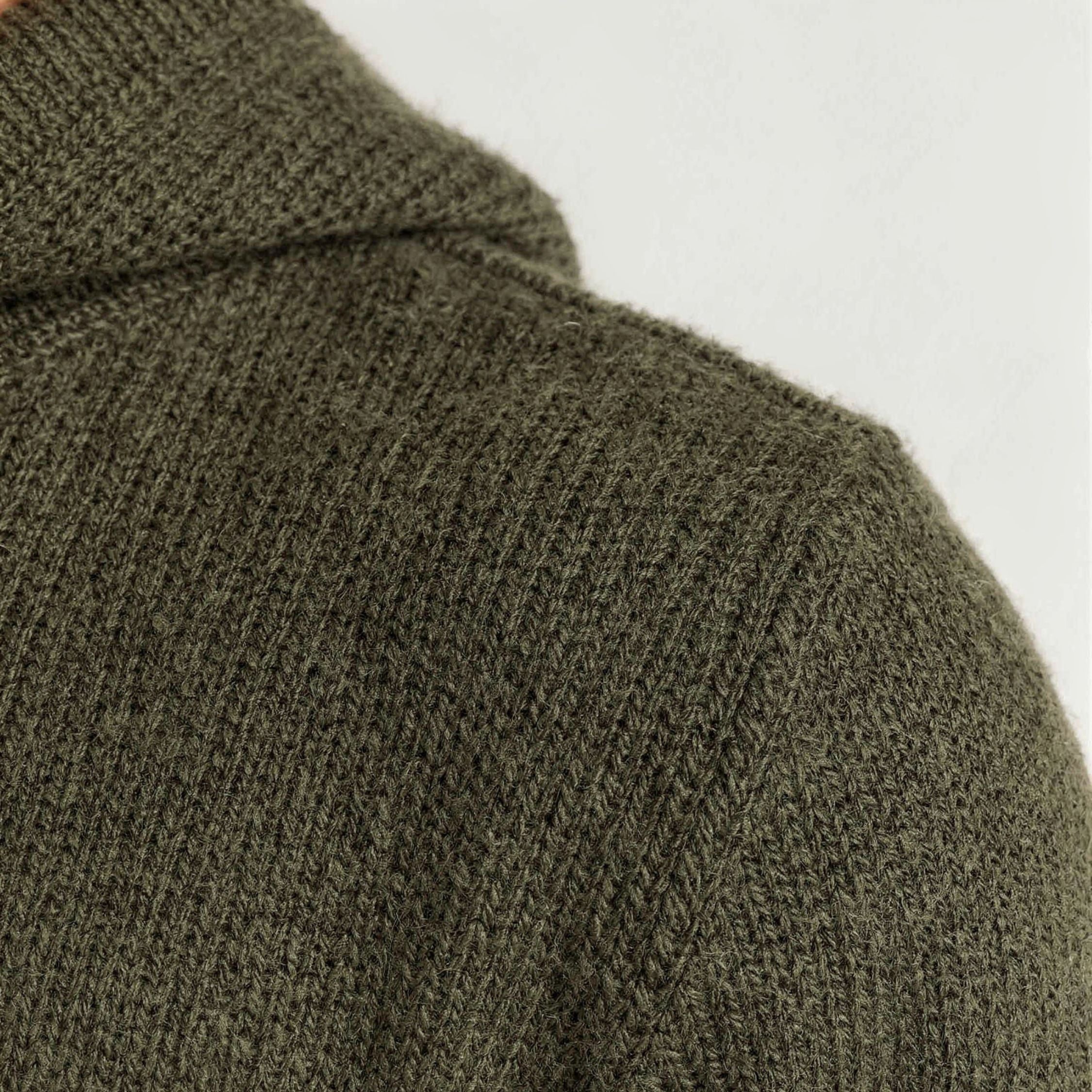 Close-up of a green knitted 100% cashmere sweater with a plain background.