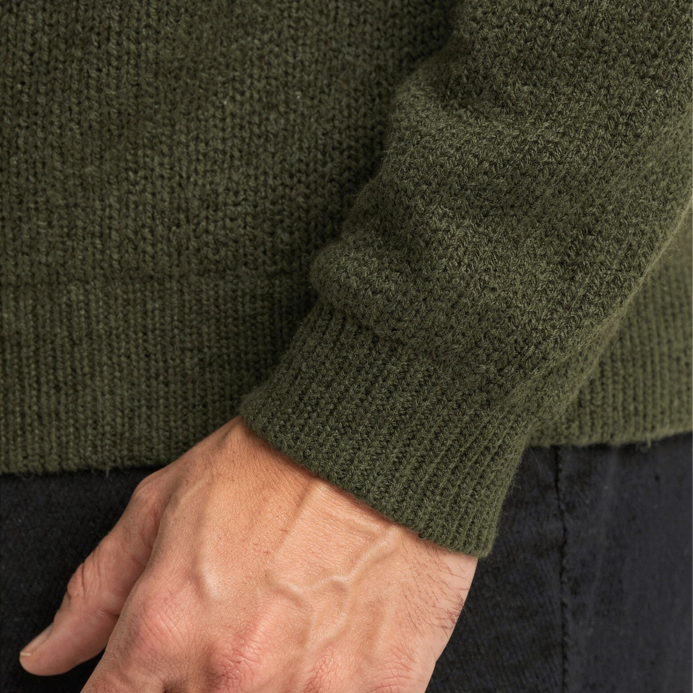Close-up of a person wearing a green 100% cashmere sweater with a hand visible.