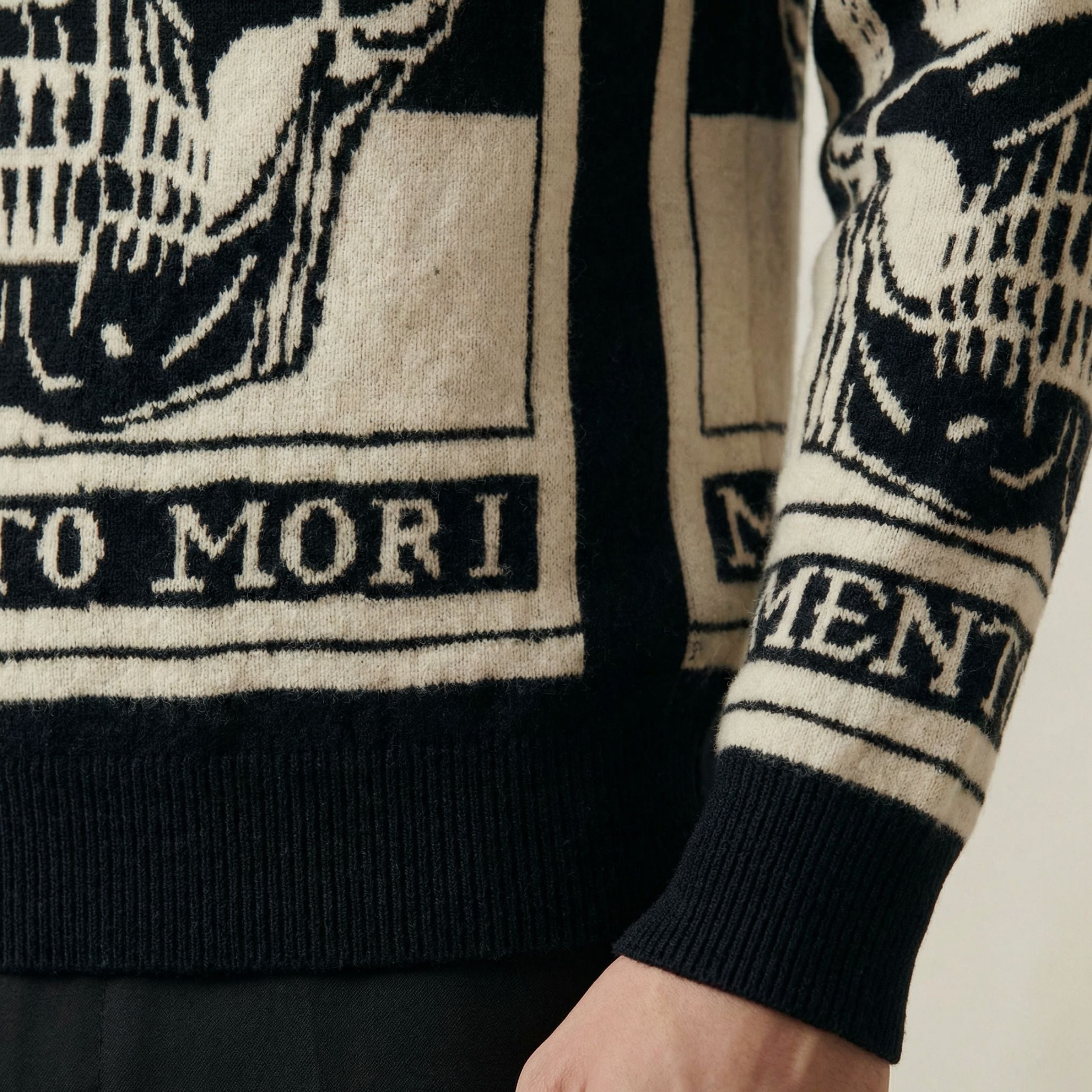 Close-up of a black and white 100% cashmere sweater with skull design and 'Memento Mori' text.