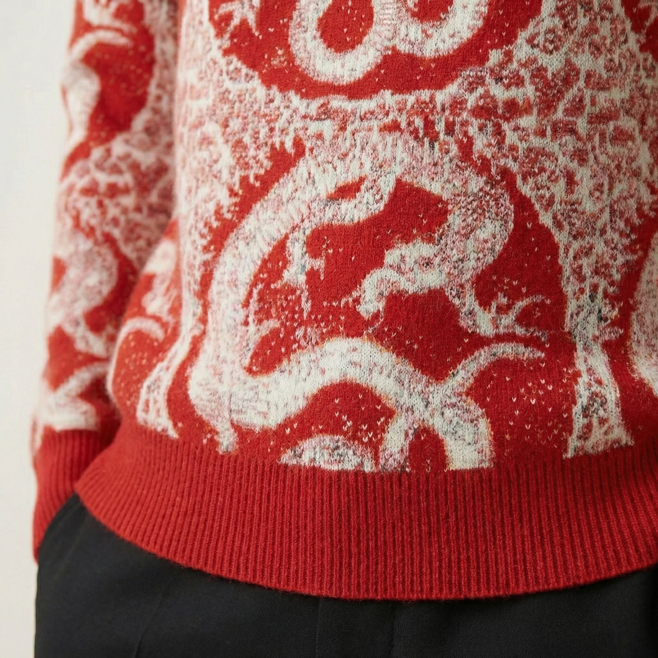 Close up of a 100% cashmere red sweater with white dragon design on a plain background