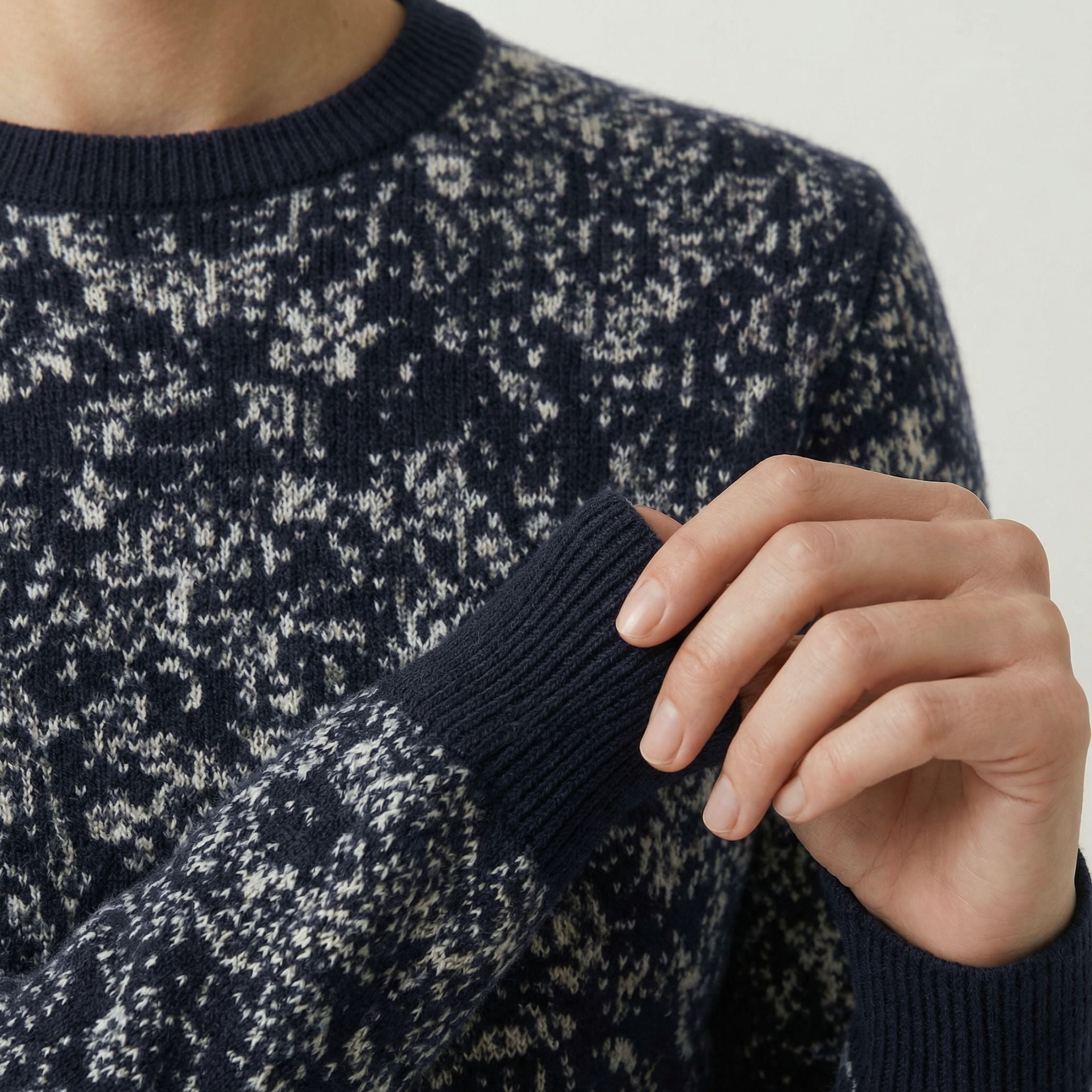 Close-up of a person wearing a patterned 100% cashmere sweater with a hand adjusting the sleeve.