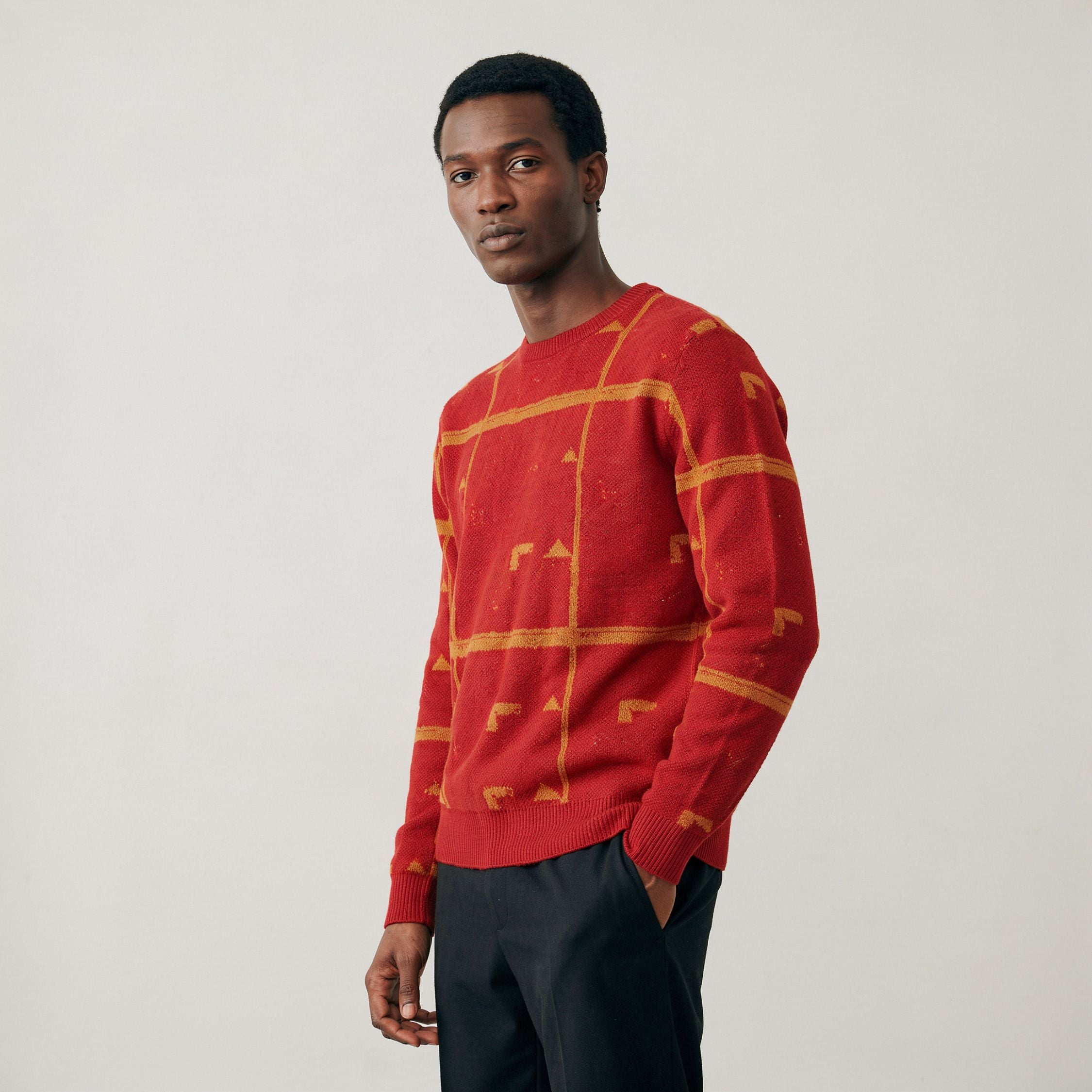 Man wearing a 100% Cashmere red sweater with geometric patterns on a plain background