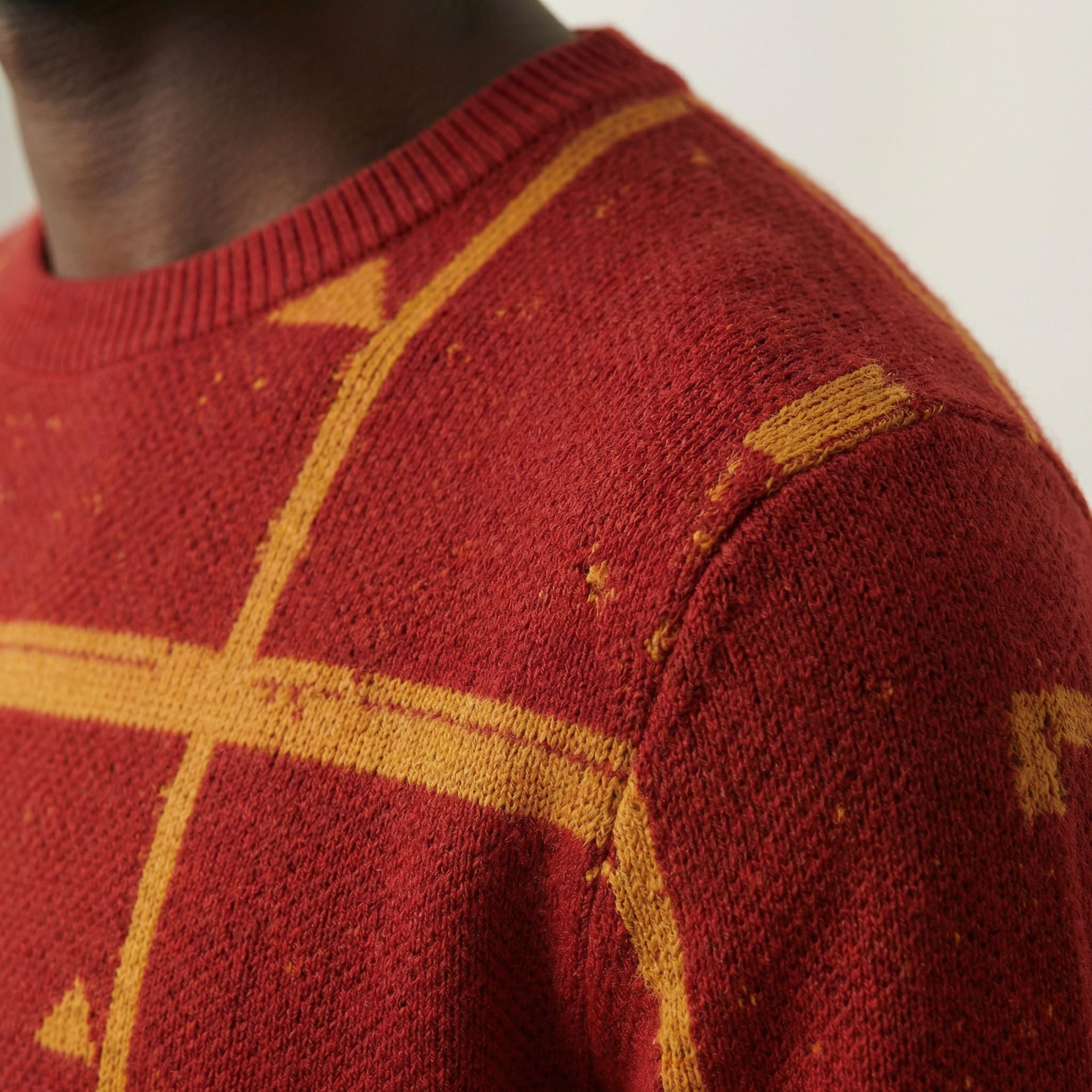 Close up macro shot of a 100% Cashmere red sweater with gold geometric patterns on a neutral background