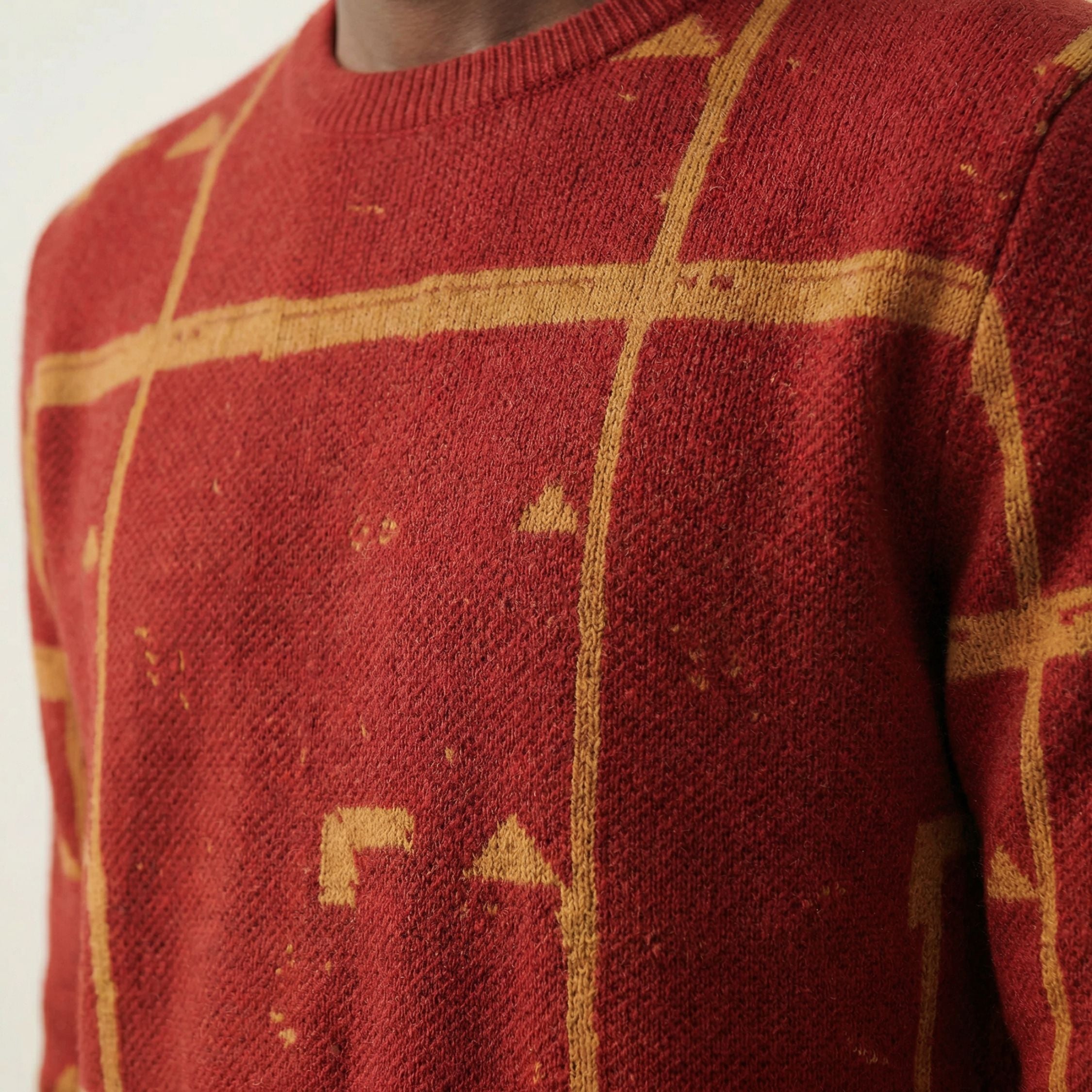 Close up macro shot of a 100% Cashmere red sweater with gold geometric patterns on a neutral background