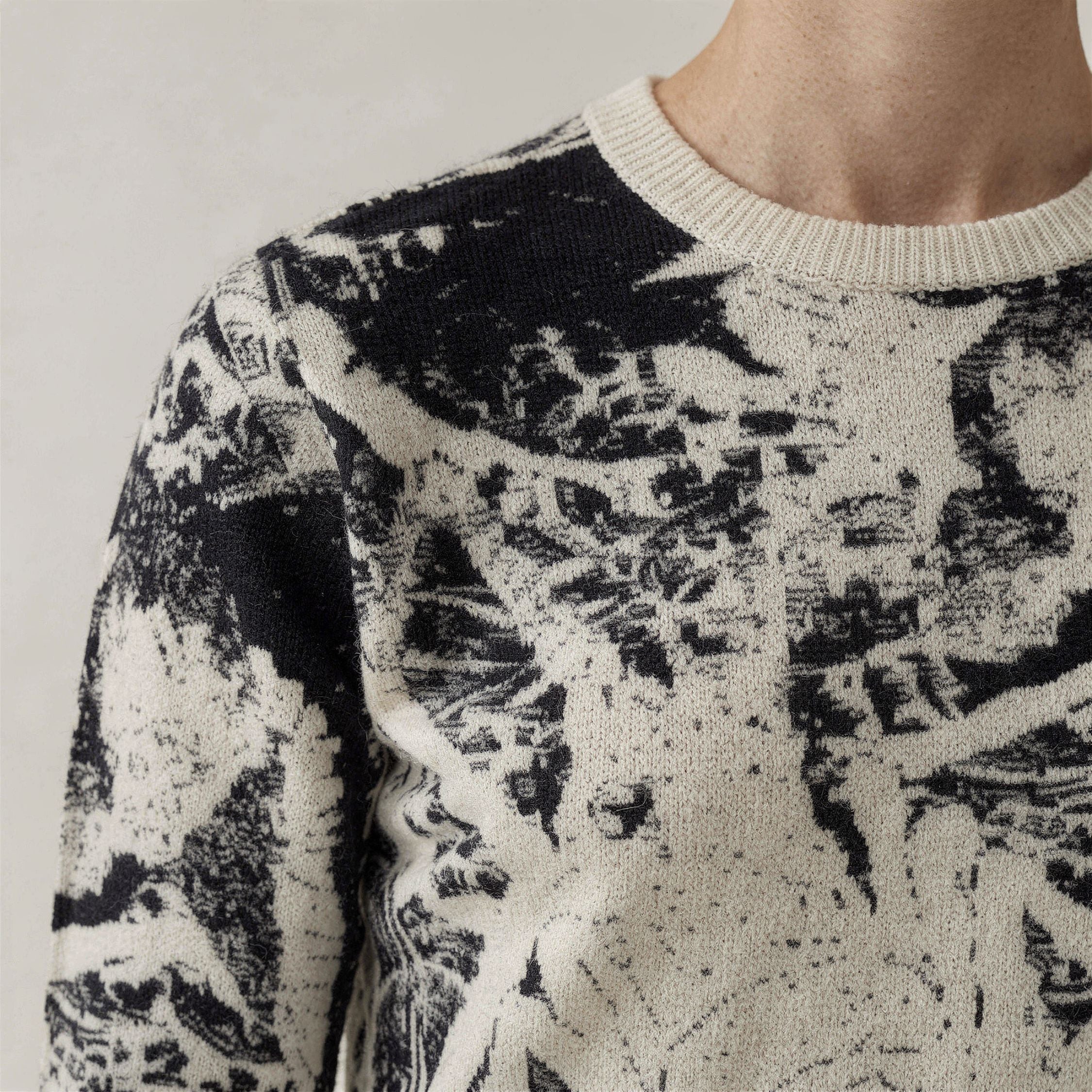Close-up of a person wearing a black and white patterned 100% cashmere sweater against a neutral background