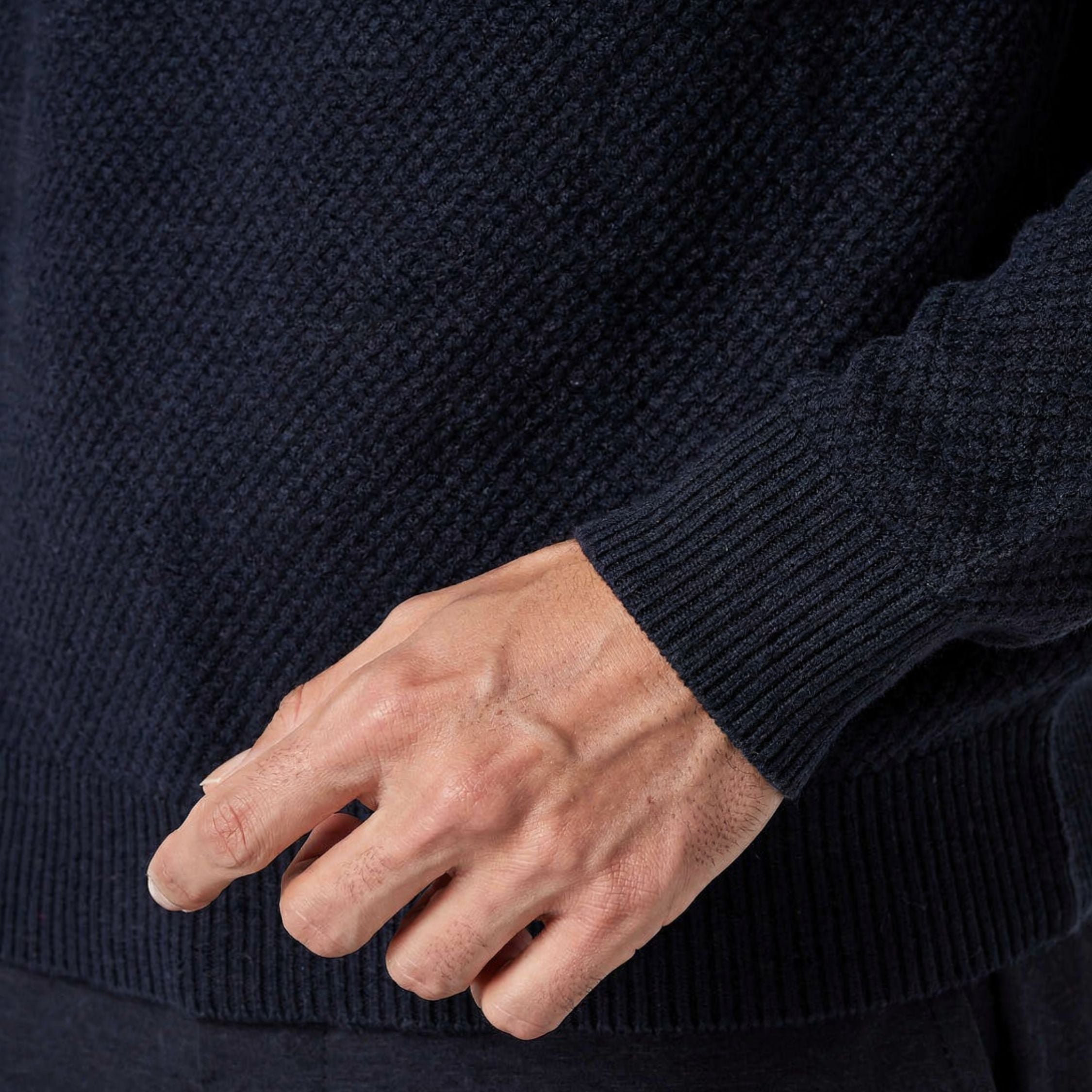 Close-up of a person wearing a 100% cashmere dark blue sweater with a hand gesture.