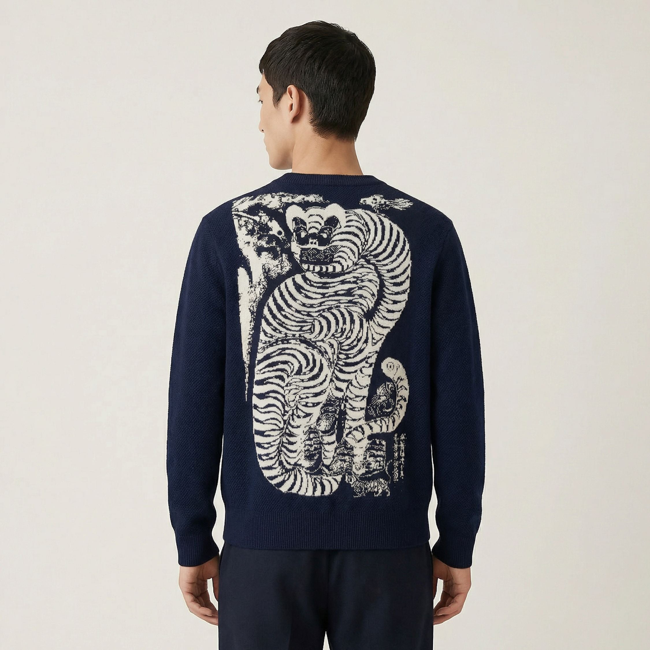 Person wearing a 100% cashmere navy sweater with a white tiger design on the back against a beige background