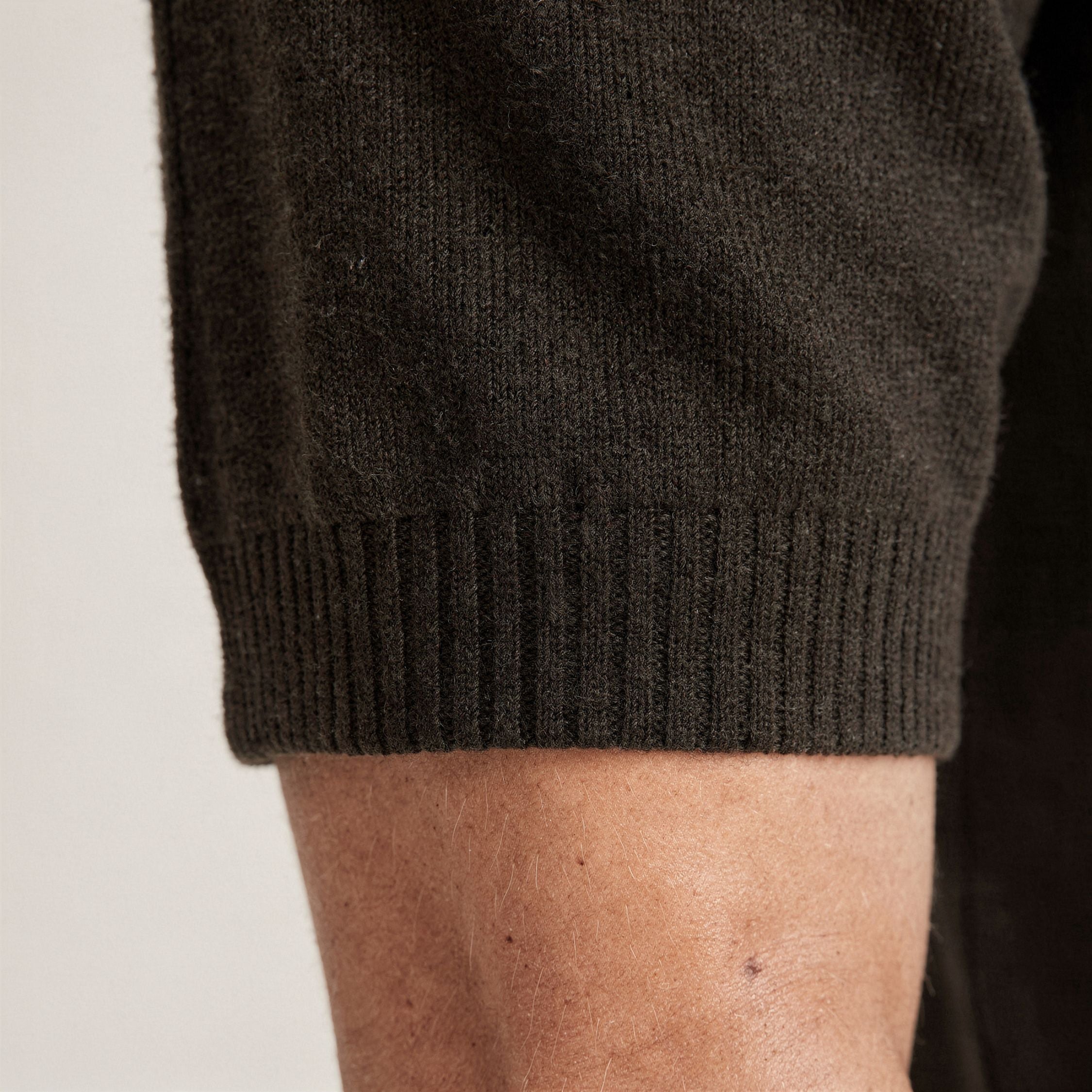Close-up of a person wearing a dark brown knitted 100% cashmere t-shirt on a light background.