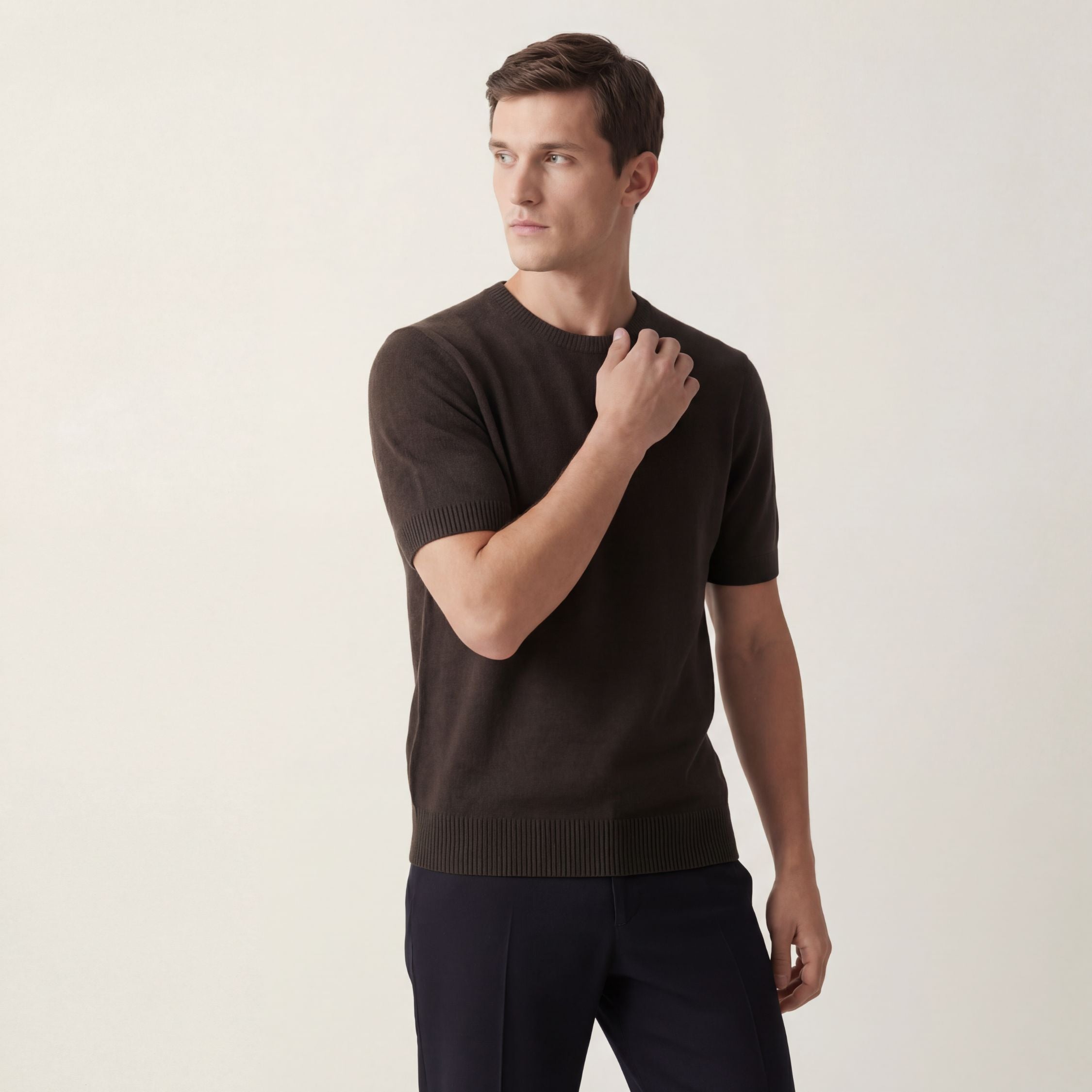 Man wearing a dark green brown t-100% cashmere knitted t-shirt and dark pants against a plain background.