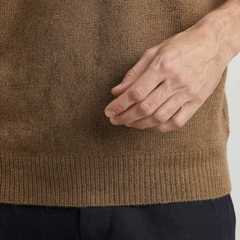 Close-up of a person wearing a brown 100% cashmere sweater with a neutral background. 