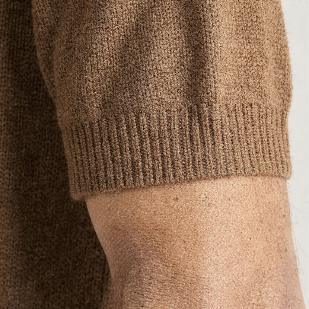 Close-up of a brown knitted 100% cashmere sweater sleeve on a person's arm against a white background.