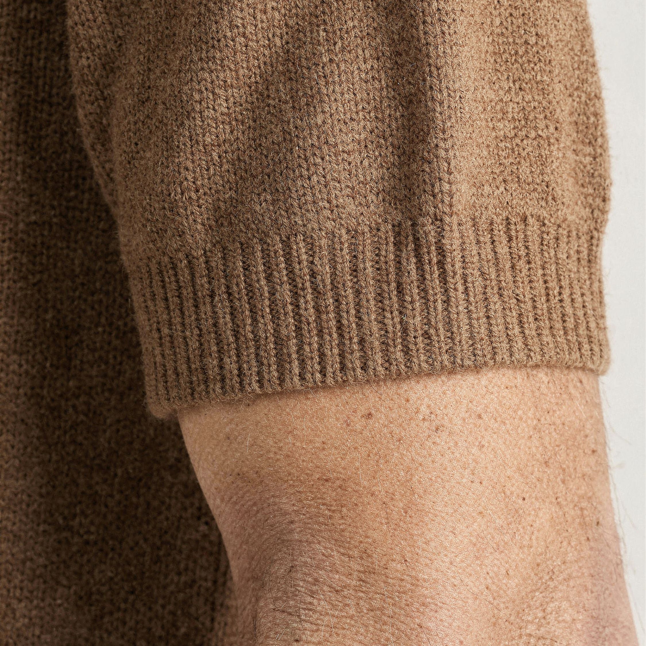 Close-up of a brown knitted 100% cashmere sweater sleeve on a person's arm against a white background.